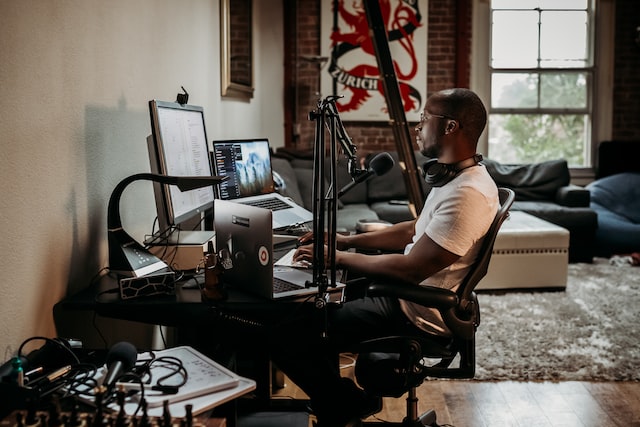 A digital creator sitting in front of his laptop and equipment, looks to be working. 
